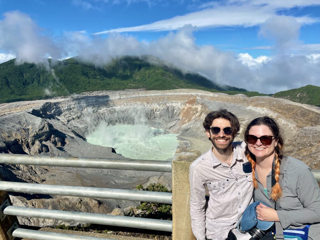 picture of a couple wearing quick dry clothing in front of a caldera filled with turquoise liquid