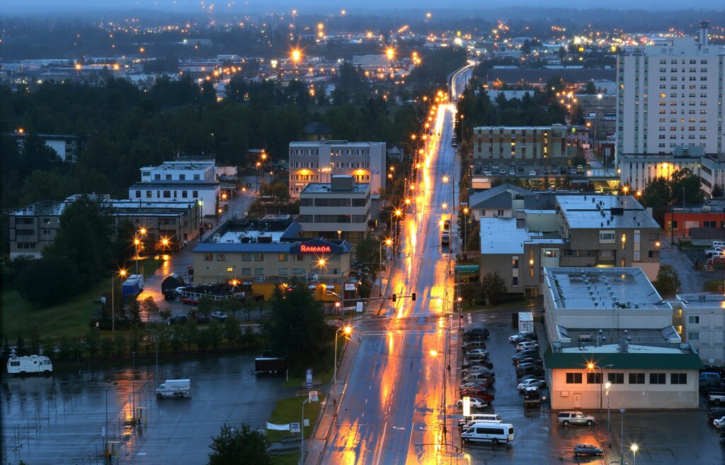 Pic of a long main street at night with buildings on either side. It is raining.