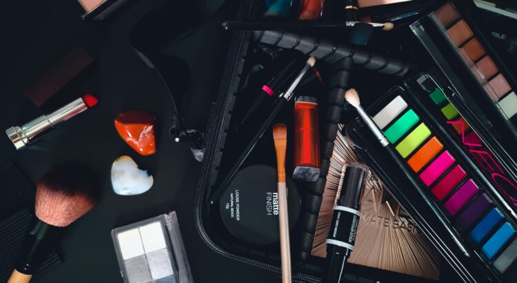Dark photo. Black background. Makeup brushes, eye shadow pallets and foundation strewn about