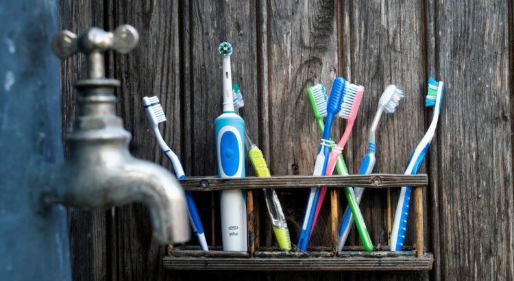 Plastic toothbrushes of various colors and an electric toothbrush sitting on a wooden shelf