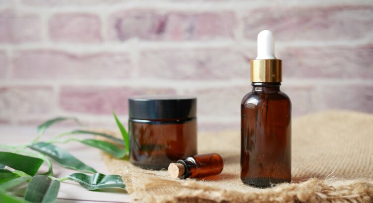 Photo of three brown glass vials on top of a light brown fabric with green leaves scattered around. The background is a brick wall.