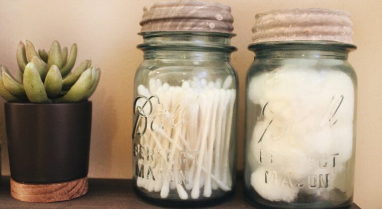 Vintage blue Ball glass jars with zinc lids hold bathroom necessities like q-tips and cotton balls on a stained black shelf which is adorned with a small potted green succulent.