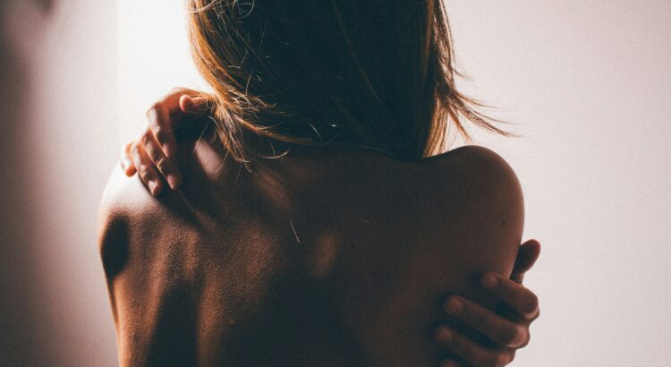 Photo of back of woman who is hugging herself. Dark setting, very shadowed.
