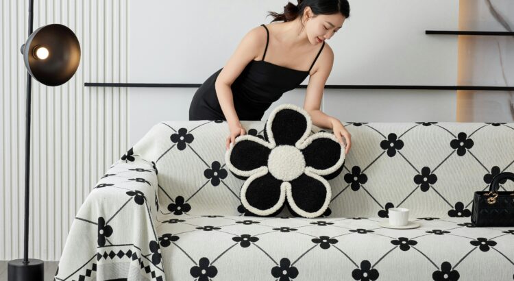 Woman with black hair in black dress putting a black flower-shaped pillow onto a black and white couch in a modernist room